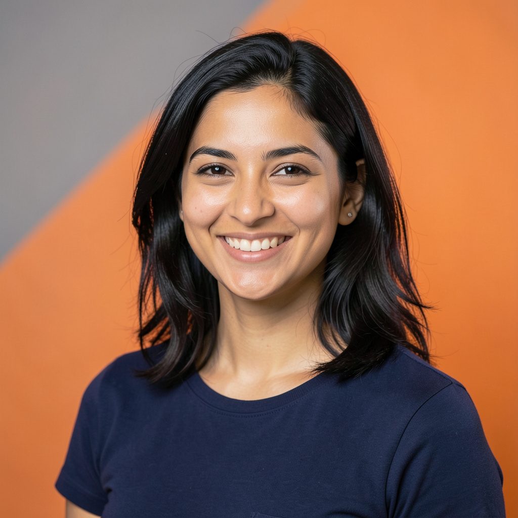 A warm studio portrait of a smiling team member with dark hair, wearing a casual navy top, photographed against a soft grey seamless backdrop.