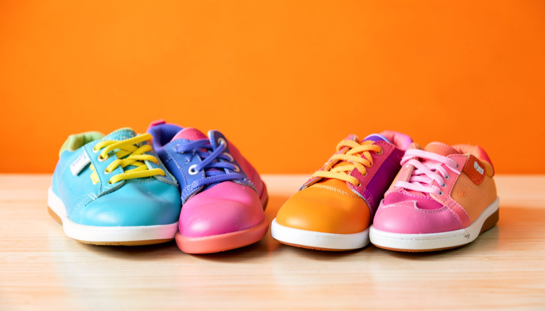 Colorful children's shoes arranged on a light wooden surface, with soft natural light and a warm, playful mood.